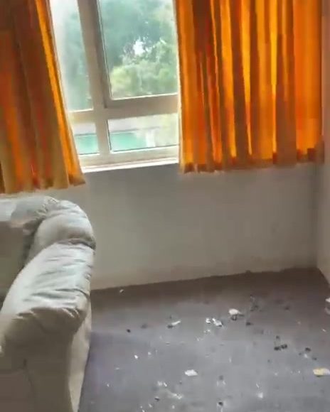The same living room emptied, with bare floor and the same orange curtains at the window