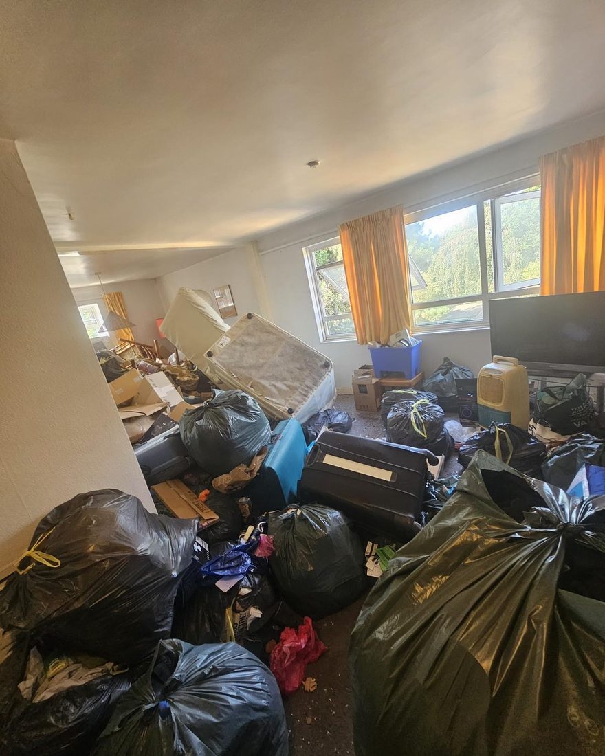 A living room filled floor to ceiling with bagged household contents, a mattress and boxes before clearance
